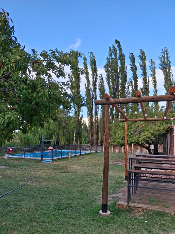 Parque con la pileta al fondo y la pérgola con mesas